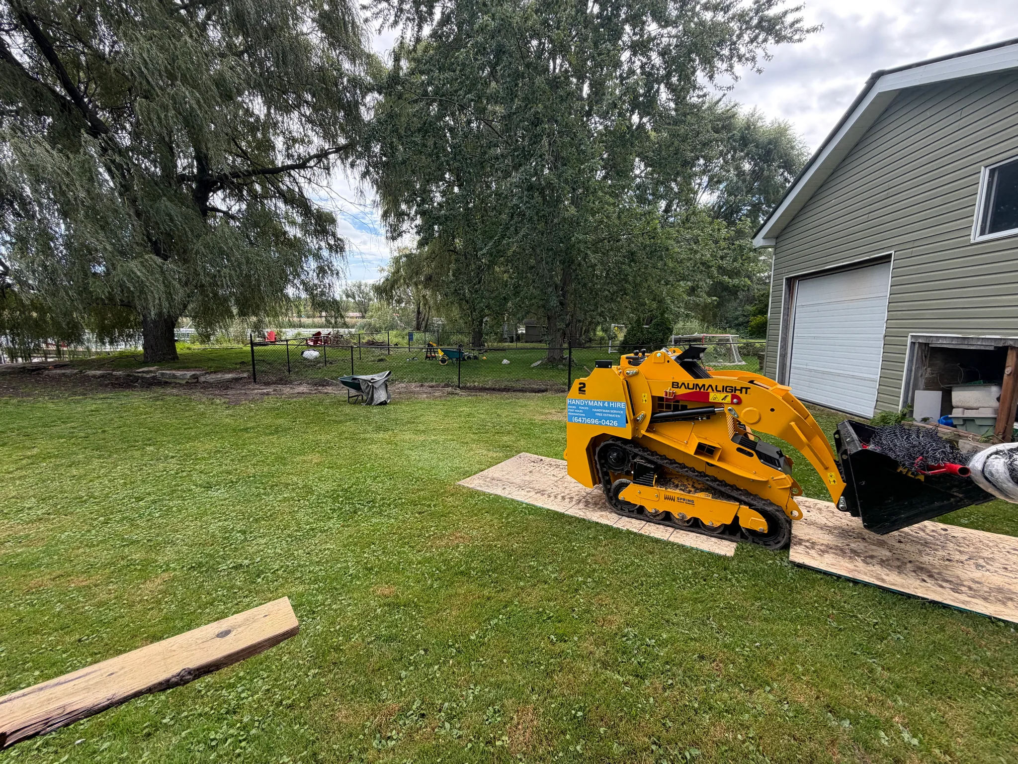 Track loader on plywood with a chain link fence job behind it